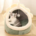 Cat lying inside a green and white pet bed with a plush ball hanging from the top.