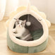 Cat lying inside a green and white pet bed with a plush ball hanging from the top.