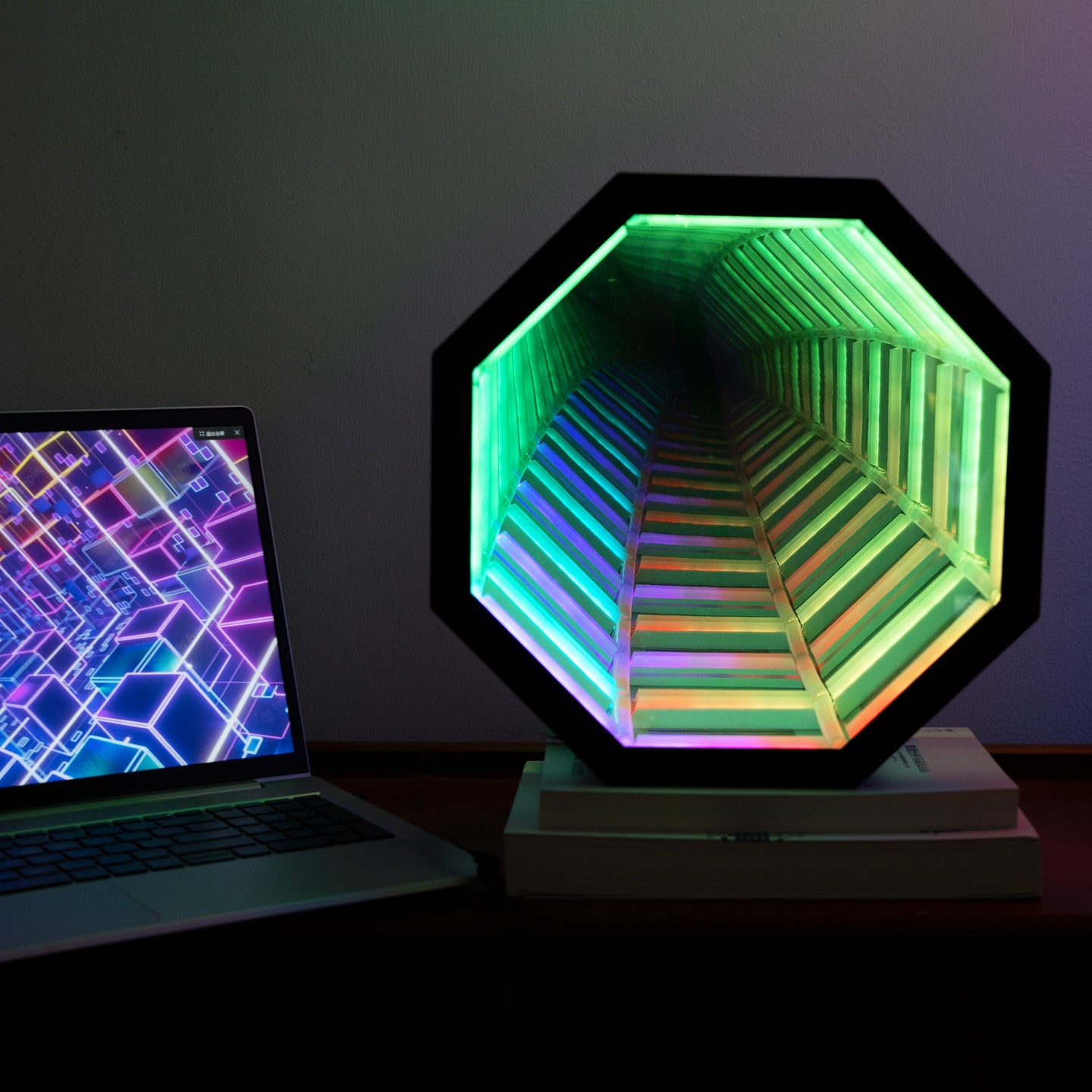 Hexagonal light fixture with colorful gradient next to a laptop on a dark surface