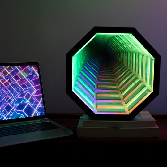 Hexagonal light fixture with colorful gradient next to a laptop on a dark surface
