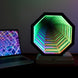 Hexagonal light fixture with colorful gradient next to a laptop on a dark surface