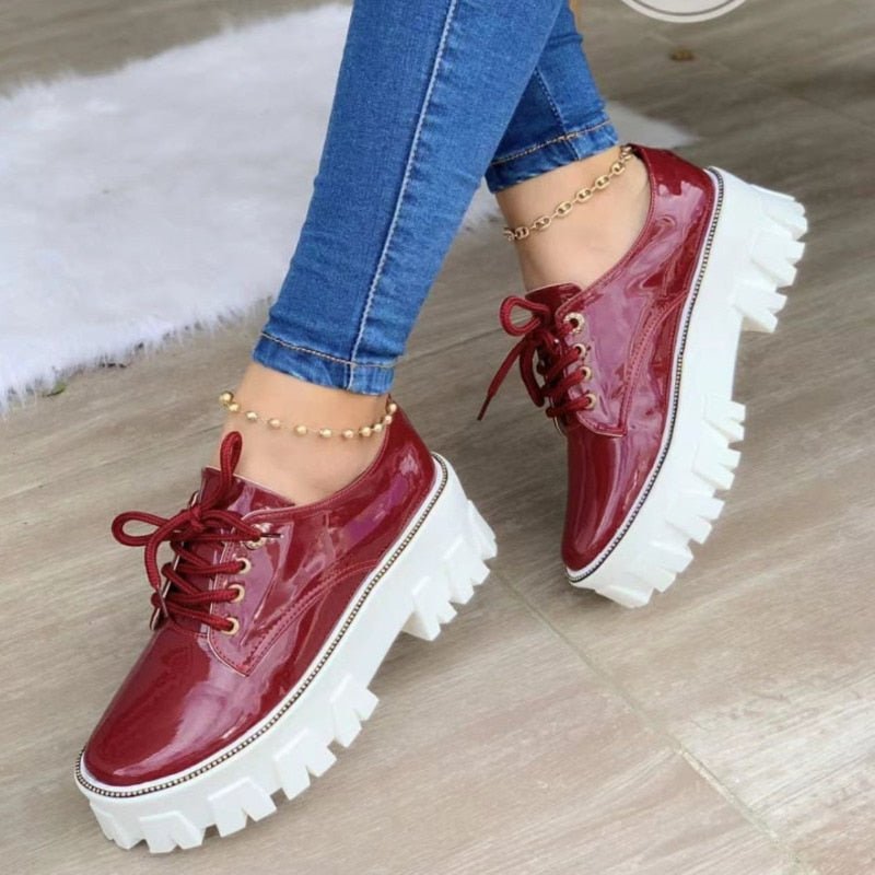 Red patent leather shoes with white soles worn with blue jeans on a light wooden floor.