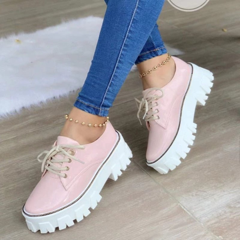 Pink platform shoes worn with blue jeans on a wooden floor.