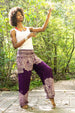 Woman in a white top and Bohemian - style purple yoga pants with floral patterns standing on a wooden path in a forest.