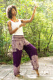 Woman in a white top and Bohemian - style purple yoga pants with floral patterns standing on a wooden path in a forest.