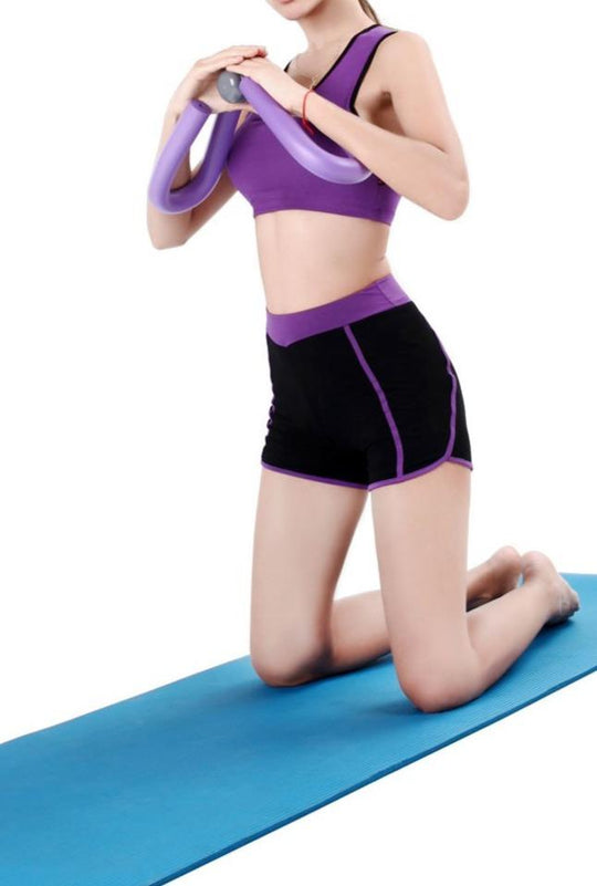 Person in purple sports bra and black shorts using a resistance band on a blue mat.