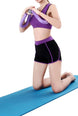 Person in purple sports bra and black shorts using a resistance band on a blue mat.